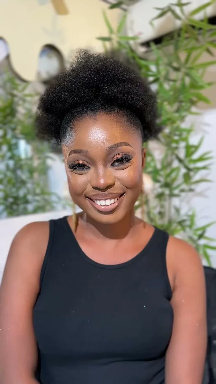 Angela smiling with a natural afro puff, in a black tank top