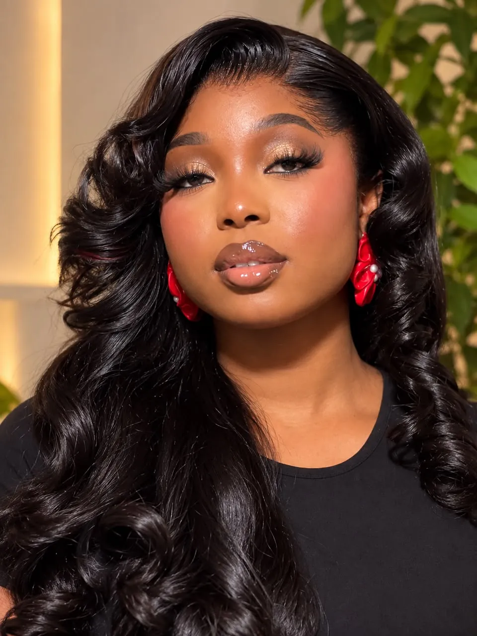 Close portrait of Angela with long glossy black waves, gold-bronze eye makeup, a brown gloss lip and red floral earrings